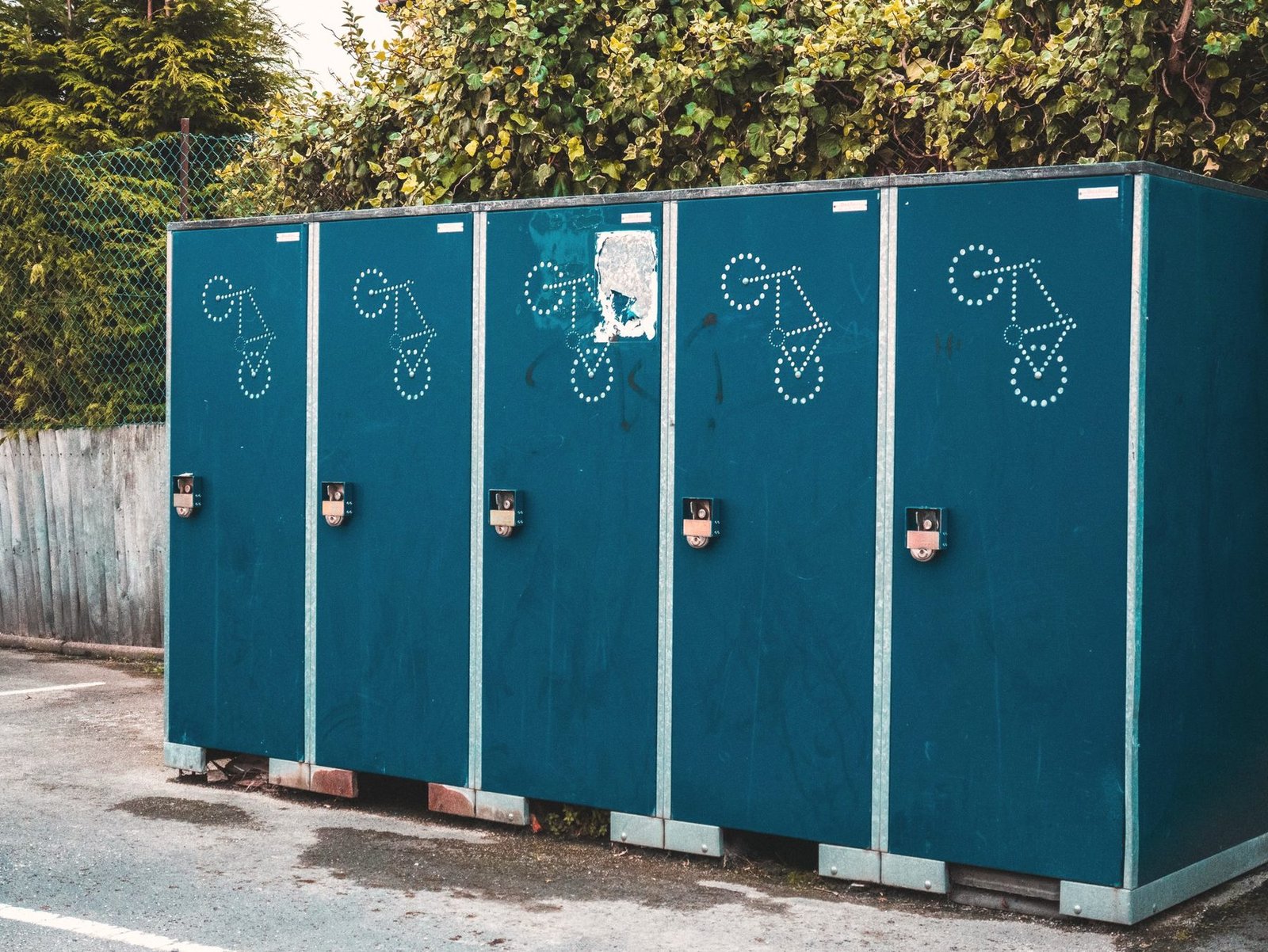 Five teal portable restroom cabins standing side by side on a paved edge.